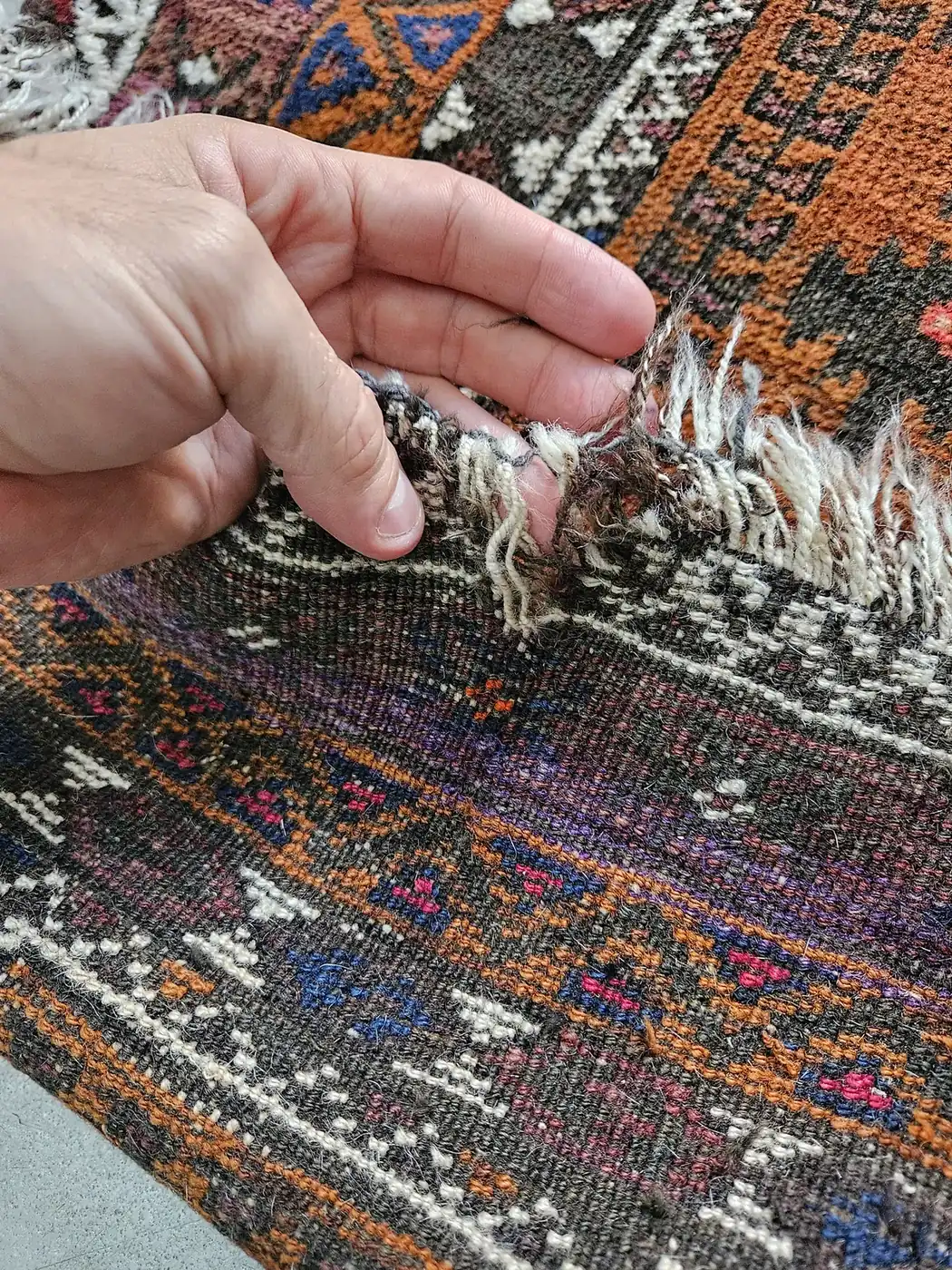 Hands working the colorful tribal fringe of an oriental rug at the repair bench